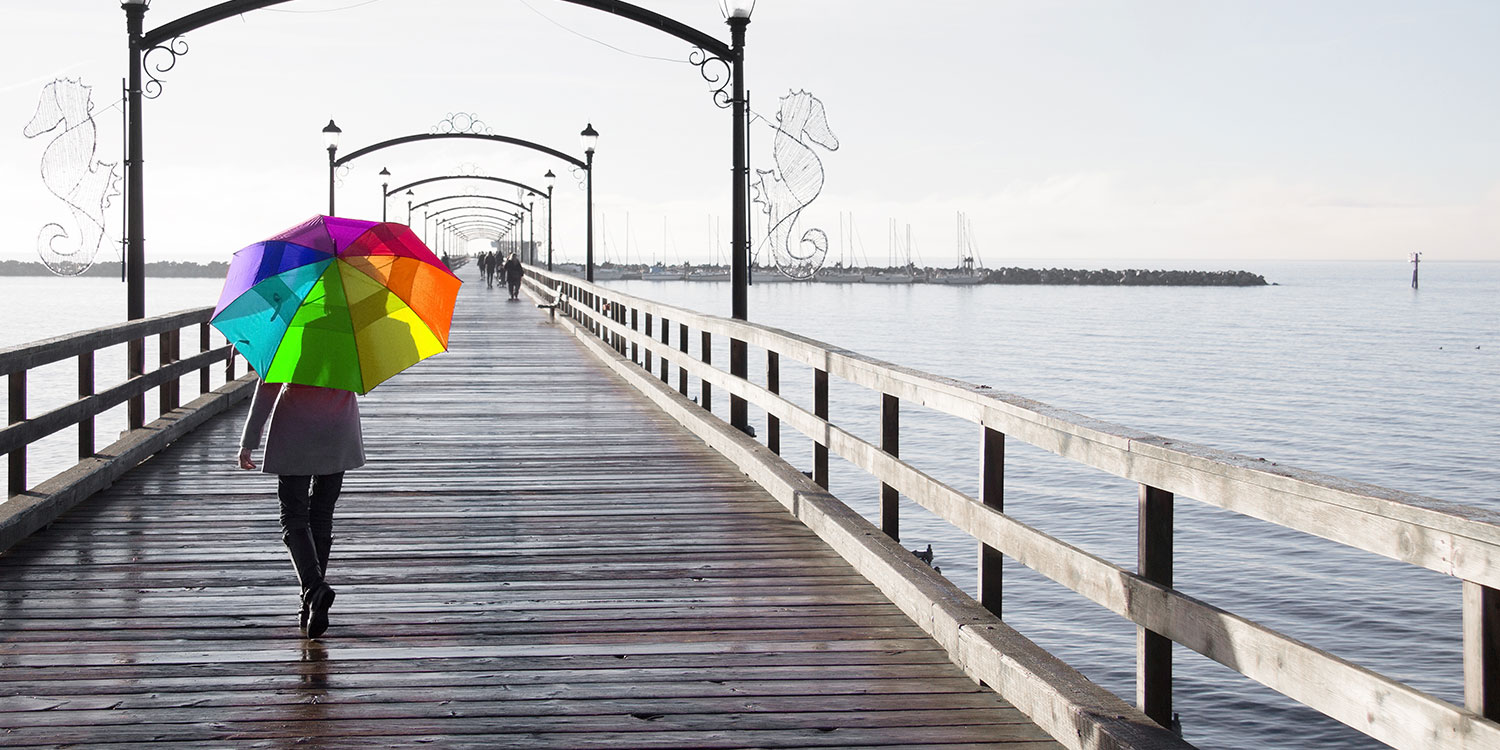Frau mit bunten Regenschirm in Regenbogenfarben läuft über eine Brücke