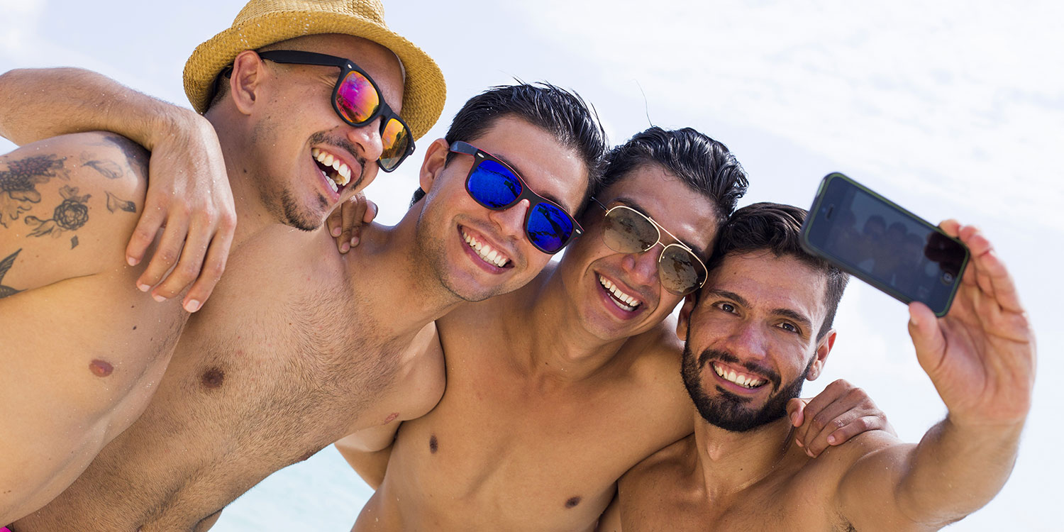Vier junge Männer mir Sonnenbrillen machen am Strand ein Selfie 