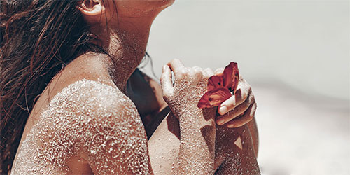 Frauenkörper mit Sand und Blume in der Hand